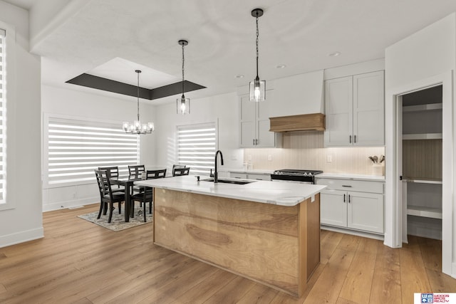 kitchen featuring stainless steel gas range oven, a raised ceiling, custom exhaust hood, light wood-type flooring, and a sink