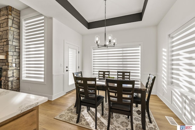 dining space with a chandelier, light wood-type flooring, a raised ceiling, and visible vents