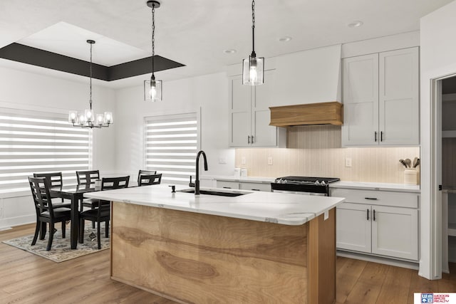 kitchen featuring wood finished floors, a kitchen island with sink, a sink, light stone countertops, and stainless steel gas range oven