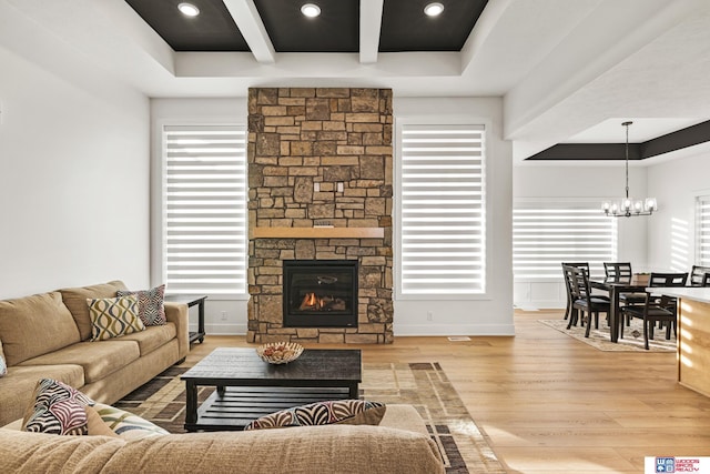 living area featuring a stone fireplace, a notable chandelier, baseboards, light wood-type flooring, and beamed ceiling