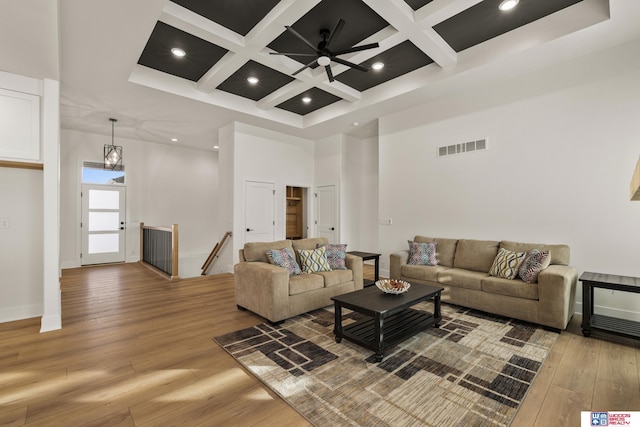 living room featuring light wood-style flooring, a high ceiling, coffered ceiling, visible vents, and beam ceiling