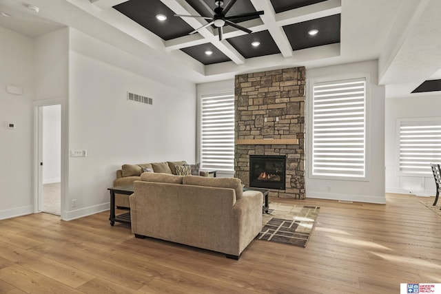 living room featuring a towering ceiling, light wood finished floors, visible vents, and a stone fireplace