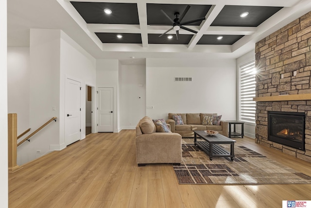 living room featuring a fireplace, visible vents, a towering ceiling, light wood-style floors, and coffered ceiling