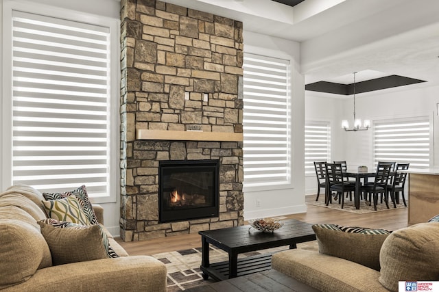 living room featuring a fireplace, a notable chandelier, baseboards, and wood finished floors