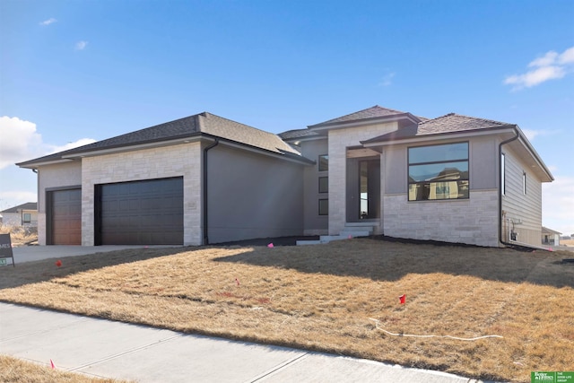 prairie-style home featuring a front yard, stone siding, roof with shingles, and an attached garage