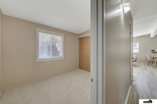 hallway featuring lofted ceiling, visible vents, and carpet flooring