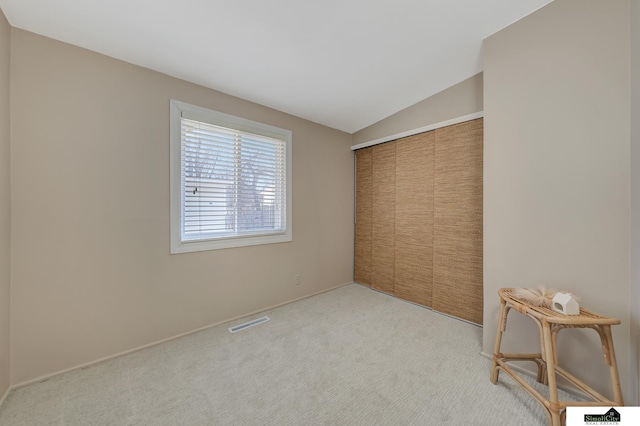 unfurnished bedroom featuring vaulted ceiling, a closet, visible vents, and light colored carpet