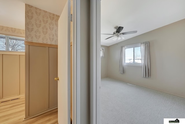 interior space with wallpapered walls, visible vents, wainscoting, ceiling fan, and vaulted ceiling