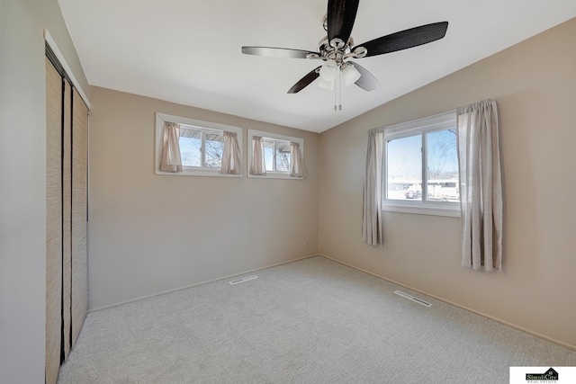 unfurnished bedroom with carpet floors, a closet, visible vents, vaulted ceiling, and ceiling fan