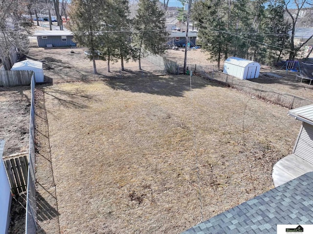 view of yard featuring a trampoline, fence, an outdoor structure, and a storage unit