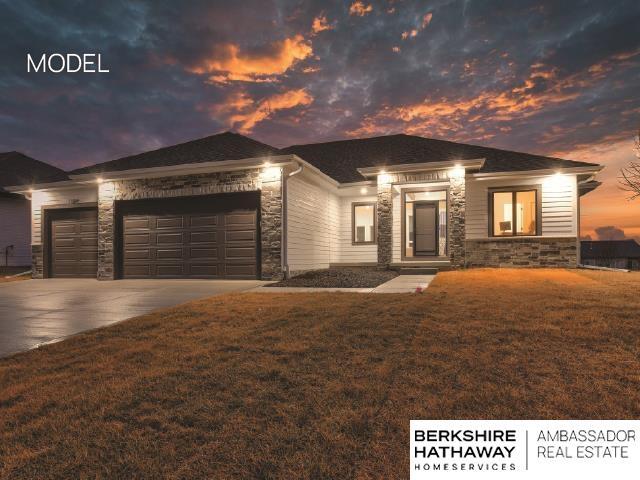 prairie-style house featuring a garage, stone siding, a front yard, and driveway