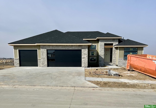 prairie-style house featuring an attached garage, stone siding, and concrete driveway