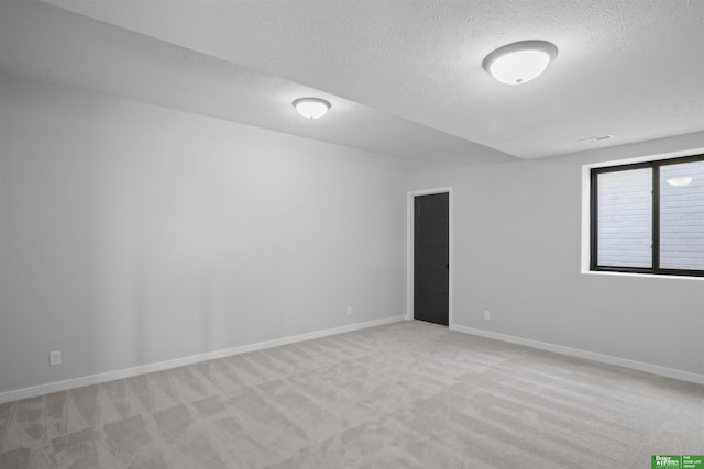 spare room with light carpet, a textured ceiling, and baseboards