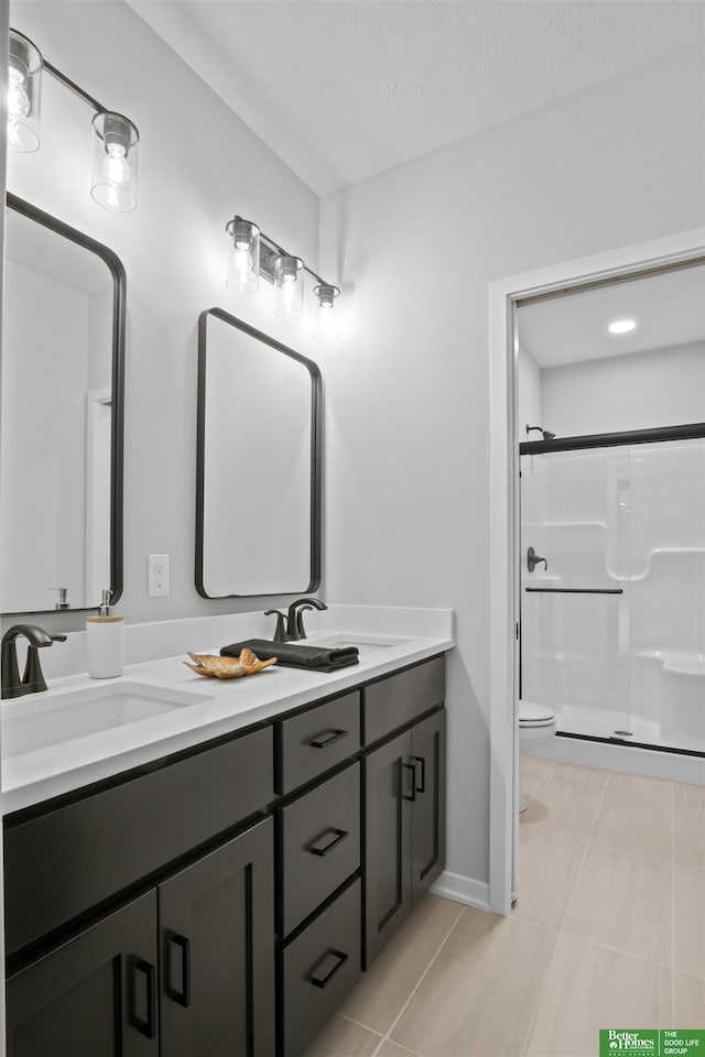 bathroom with a stall shower, a sink, toilet, and double vanity