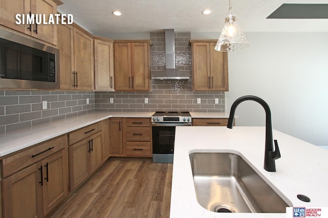 kitchen with wood finished floors, a sink, light countertops, appliances with stainless steel finishes, and wall chimney range hood