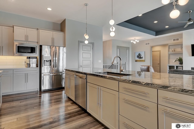 kitchen featuring decorative light fixtures, stainless steel appliances, visible vents, a sink, and dark stone counters