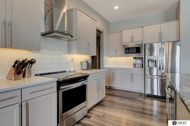 kitchen with tasteful backsplash, wall chimney exhaust hood, light stone counters, wood finished floors, and stainless steel appliances