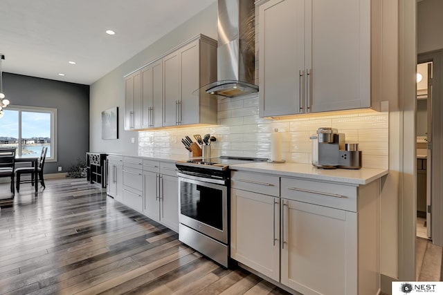 kitchen featuring wall chimney range hood, stainless steel range with electric stovetop, tasteful backsplash, and wood finished floors