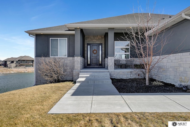 property entrance with stone siding, roof with shingles, and a lawn