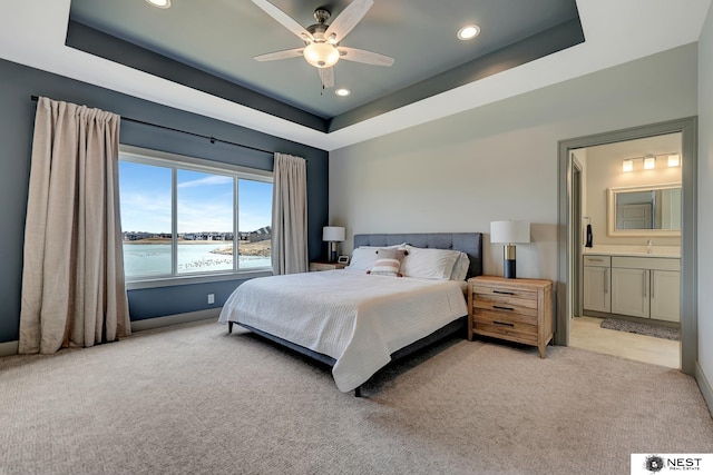 bedroom with light carpet, a tray ceiling, and a sink