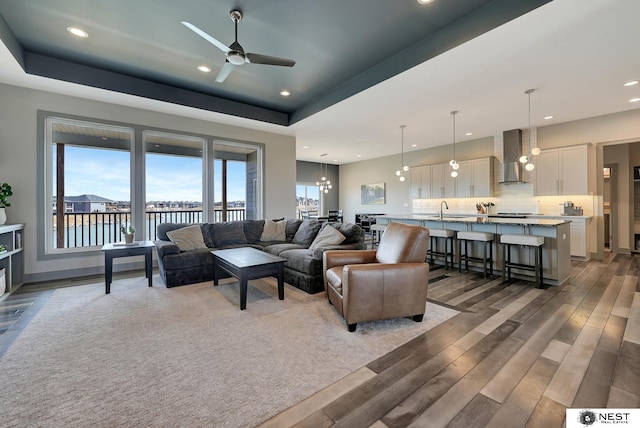 living area with ceiling fan with notable chandelier, a raised ceiling, wood finished floors, and recessed lighting