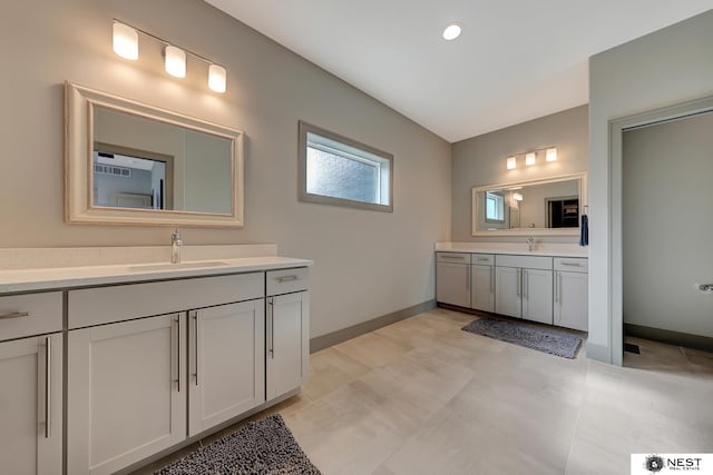 bathroom featuring baseboards, two vanities, and a sink