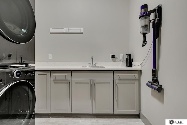 washroom featuring stacked washer and dryer, cabinet space, and a sink