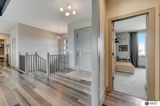 hall featuring a chandelier, wood finished floors, an upstairs landing, and baseboards