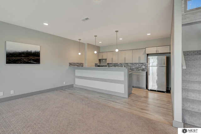 kitchen with tasteful backsplash, visible vents, freestanding refrigerator, a peninsula, and pendant lighting