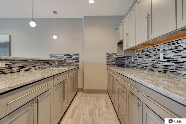 kitchen with pendant lighting, light wood-style flooring, backsplash, a sink, and light stone countertops