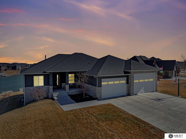 view of front facade with concrete driveway, stone siding, roof with shingles, an attached garage, and a yard