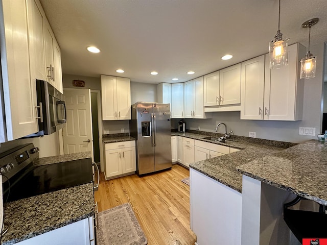 kitchen with light wood finished floors, white cabinets, appliances with stainless steel finishes, a peninsula, and a sink