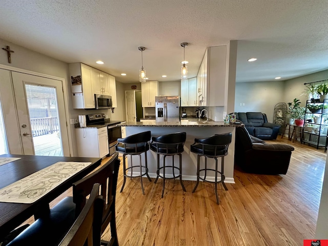 kitchen with a peninsula, white cabinetry, open floor plan, appliances with stainless steel finishes, and light wood-type flooring