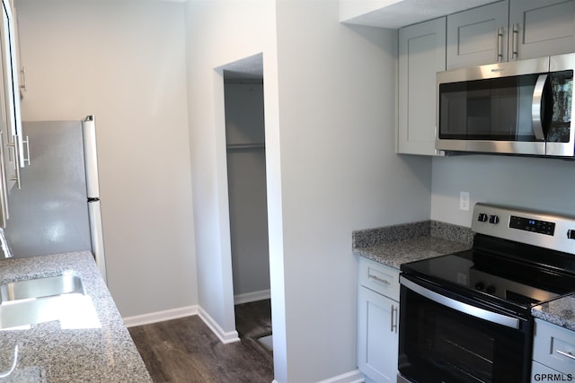 kitchen featuring stainless steel appliances, dark wood-style flooring, a sink, and baseboards