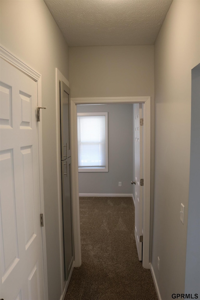 hall with a textured ceiling, dark carpet, and baseboards