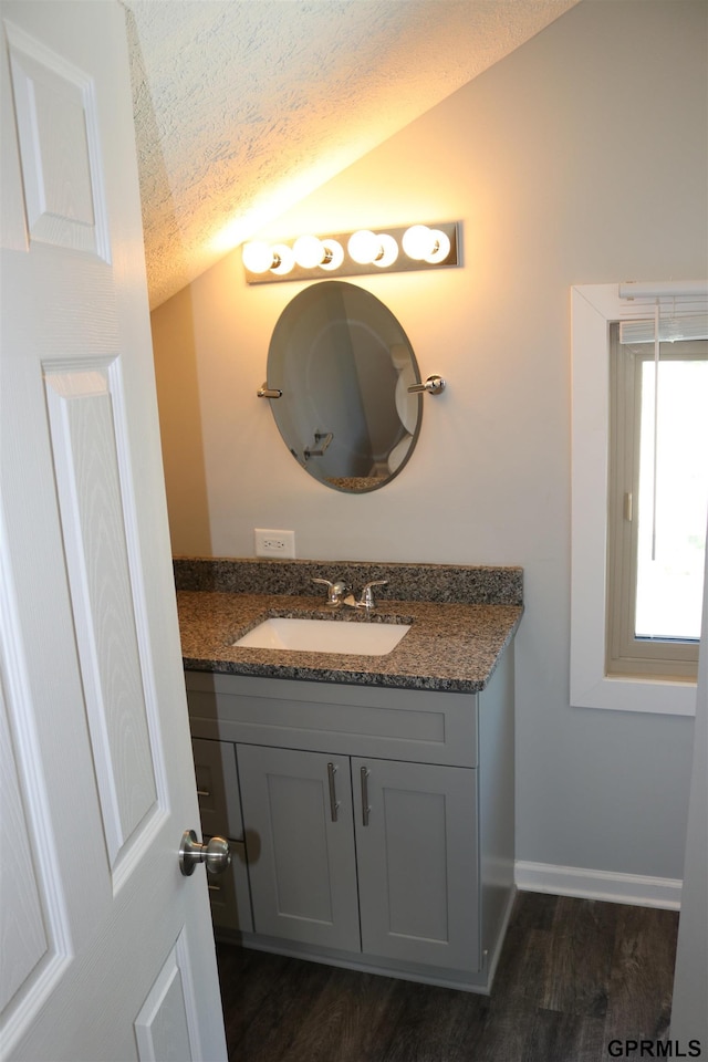 bathroom with lofted ceiling, a textured ceiling, vanity, wood finished floors, and baseboards