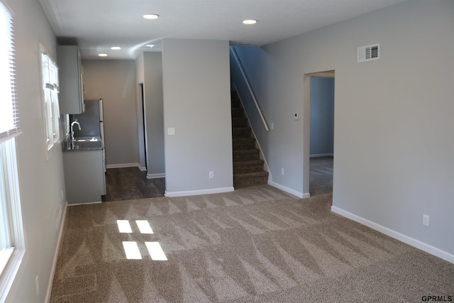 unfurnished living room with carpet, visible vents, a sink, and stairs