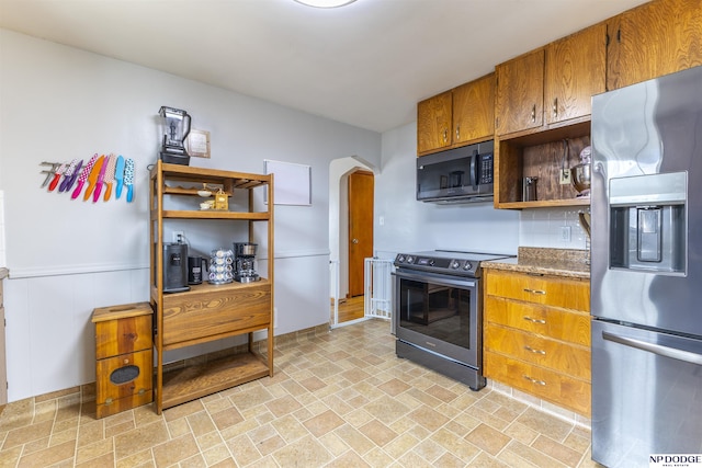 kitchen featuring arched walkways, brown cabinets, open shelves, appliances with stainless steel finishes, and stone finish flooring