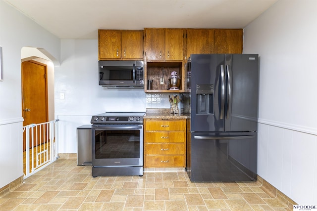 kitchen with a wainscoted wall, electric range, open shelves, black refrigerator with ice dispenser, and brown cabinetry