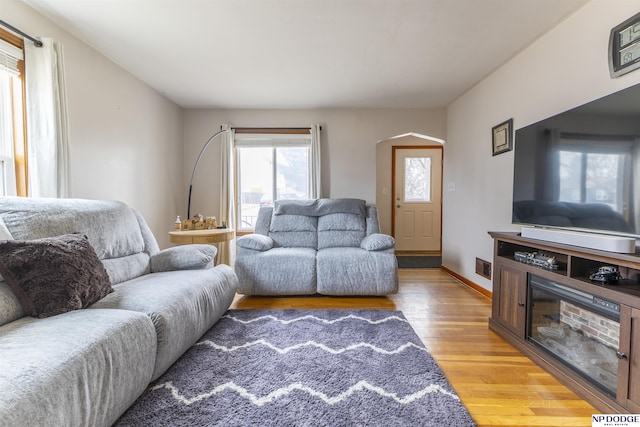 living area featuring light wood-style floors, baseboards, visible vents, and arched walkways