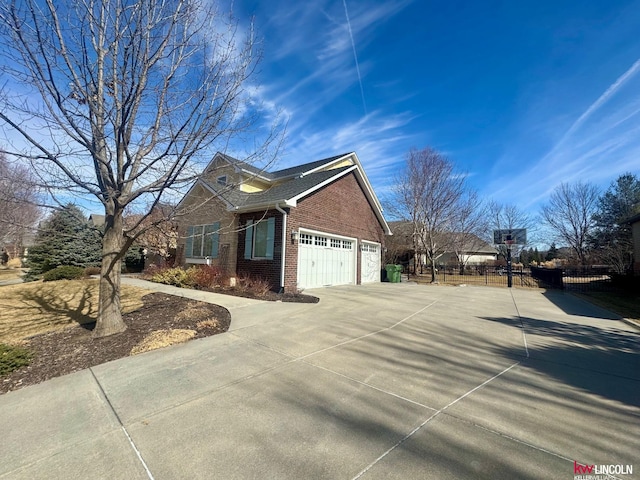 view of side of property featuring a garage, driveway, brick siding, and fence