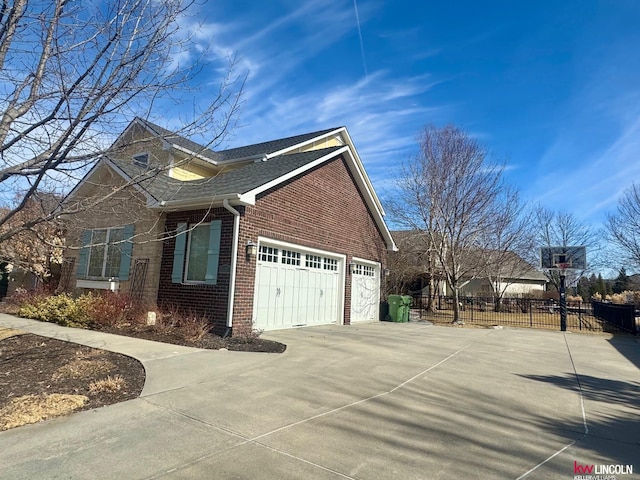 view of side of property featuring a garage, concrete driveway, roof with shingles, fence, and brick siding