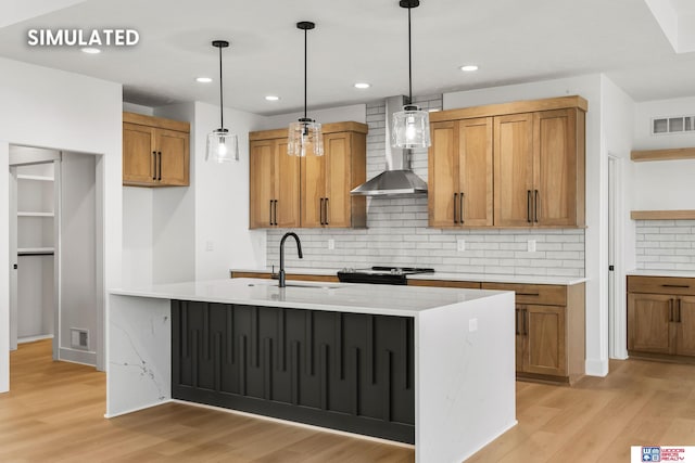 kitchen featuring visible vents, brown cabinetry, wall chimney exhaust hood, light wood-style floors, and a sink