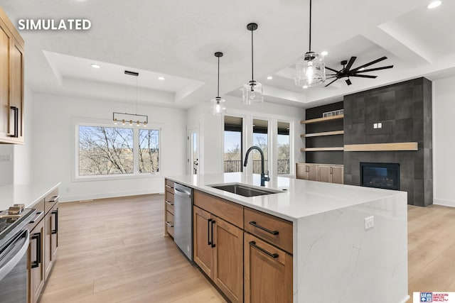 kitchen featuring a tray ceiling, a fireplace, stainless steel appliances, a sink, and light wood-type flooring