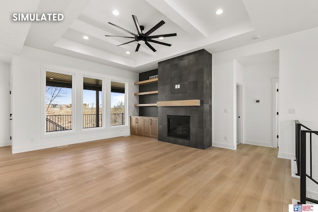 unfurnished living room with light wood-type flooring, a tray ceiling, a fireplace, and baseboards