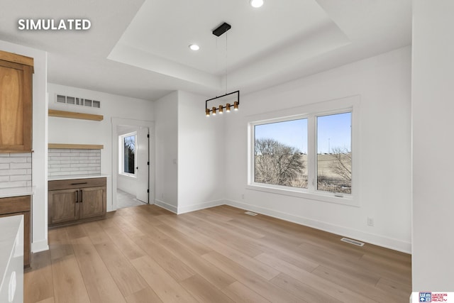 unfurnished dining area with light wood finished floors, visible vents, and a raised ceiling