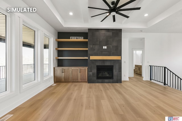 unfurnished living room featuring light wood-type flooring, a tray ceiling, visible vents, and a tiled fireplace