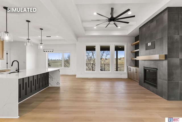 unfurnished living room with light wood-type flooring, a tiled fireplace, a tray ceiling, and a sink