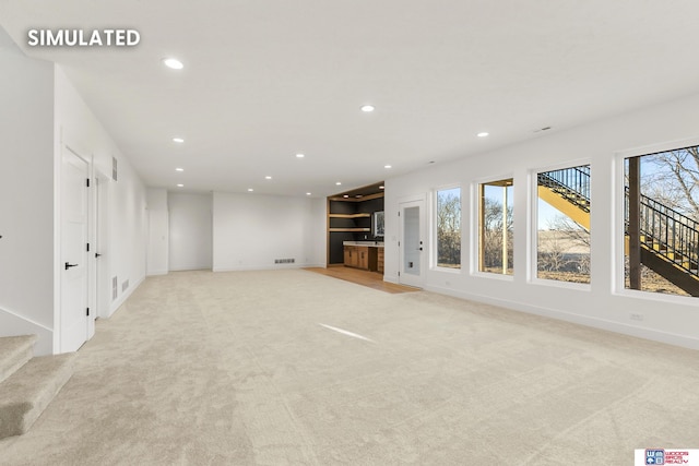 unfurnished living room with light carpet, plenty of natural light, stairway, and recessed lighting