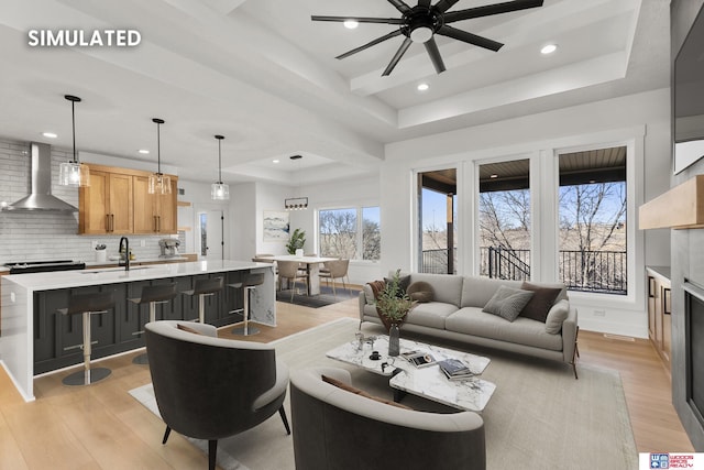 living room with a tray ceiling, a glass covered fireplace, light wood finished floors, and recessed lighting